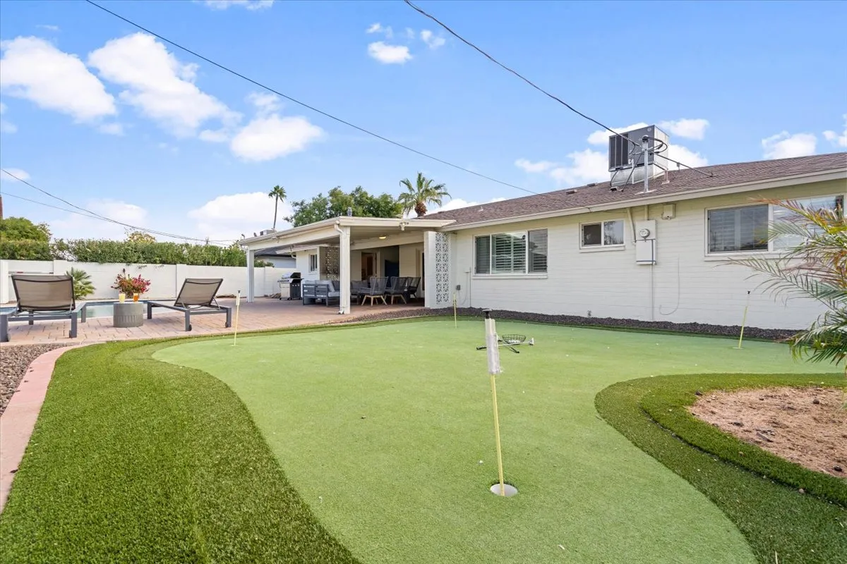 A well-maintained putting green set beside a covered patio area, with plush outdoor seating and stylish decor. The scene suggests leisurely mornings or fun afternoons practicing golf steps from the comfort of your patio.