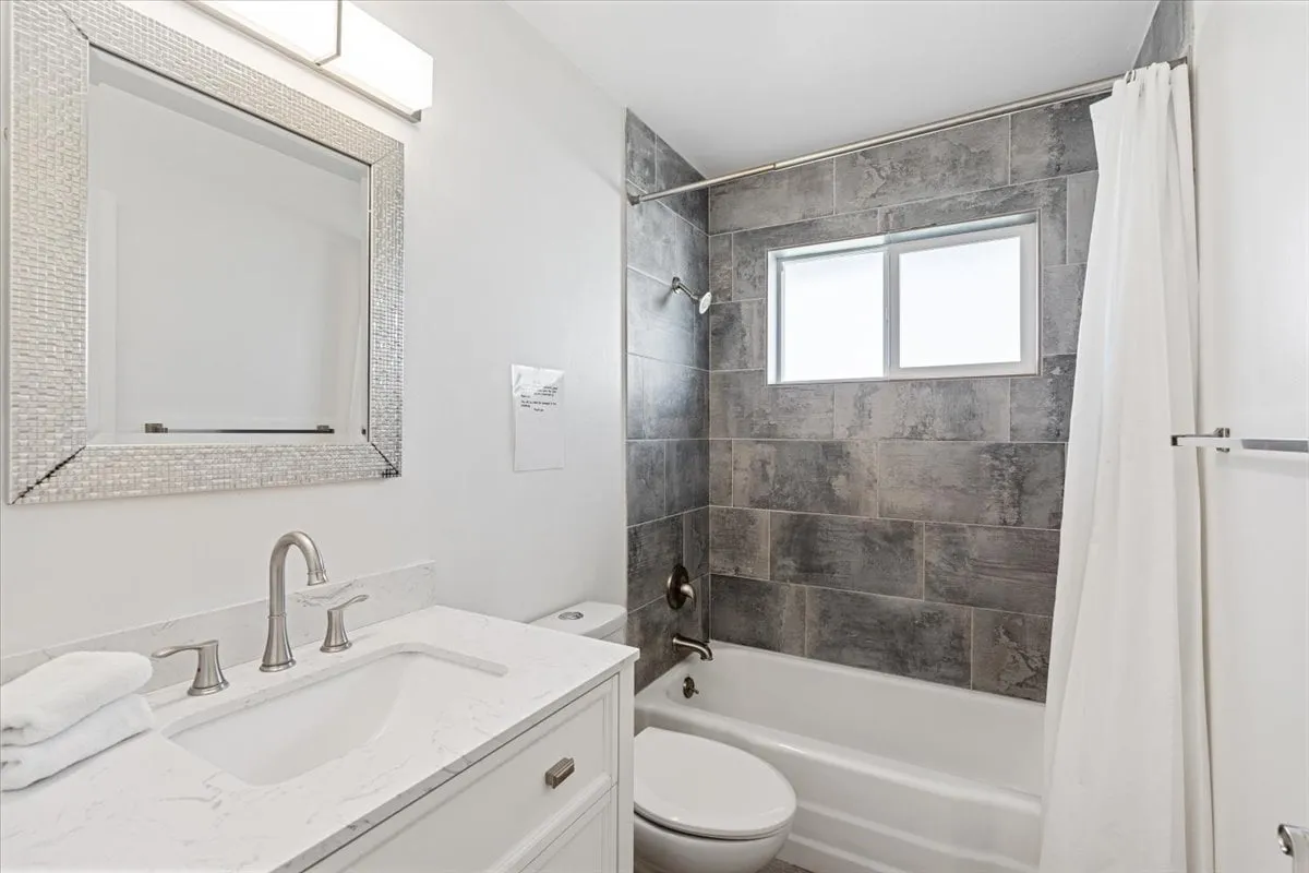A fresh, inviting bathroom with a vanity and sink, mirrored frame, and a shower with curtain, highlighted by natural light from a window. The overall vibe is clean and calming, ideal for relaxing after travel or preparing for the day ahead.
