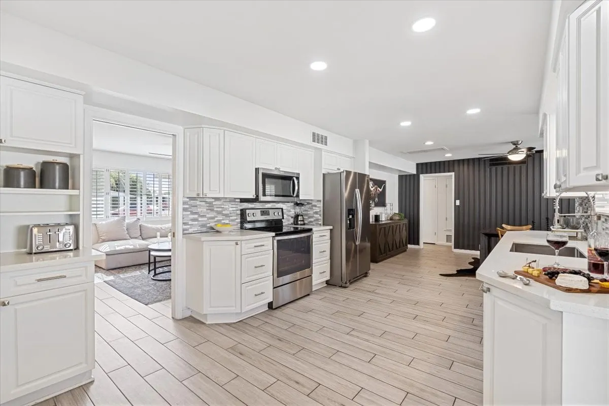A modern kitchen is shown with stylish cabinetry, stainless steel appliances, a kitchen island with seating, and an open doorway that extends into the living area. It visually unites the food prep and communal zones, underlining the open-plan concept.