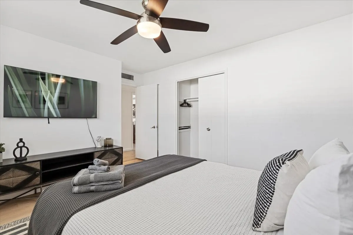 A welcoming bedroom with a bed neatly arranged with towels, a large wall-mounted TV, and a black dresser adorned with decorative items. The room feels cozy and well-prepared for guests to unwind or enjoy entertainment from bed.