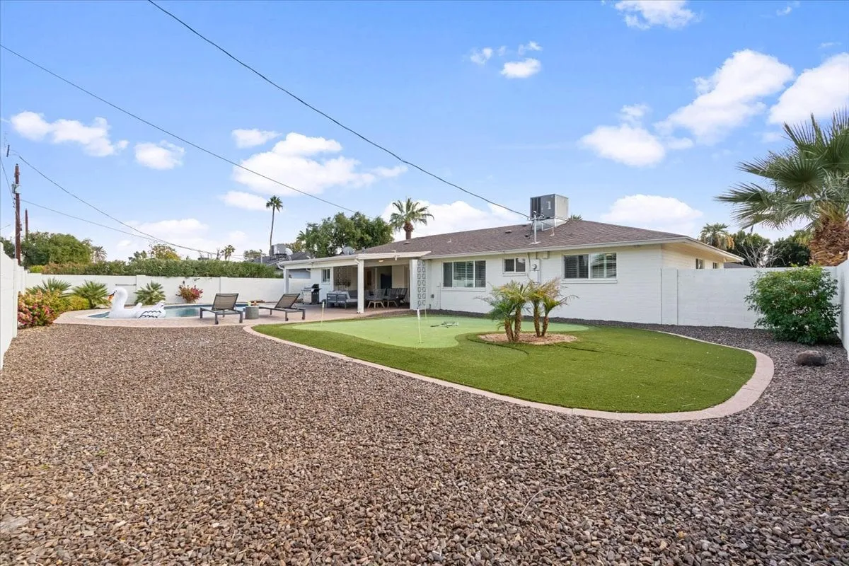 A broad exterior view of a backyard retreat, highlighting a well-maintained swimming pool, lush lawn area, comfortable patio seating, and landscaped plants. The layout encourages both group interaction and quiet moments, ideal for team-building or winding down after meetings.