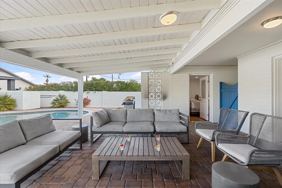 A stylish outdoor seating area overlooks a sparkling swimming pool, framed by decorative walls and lush landscaping. The setup invites relaxation and socializing, ideal for sunset gatherings or poolside parties with friends.