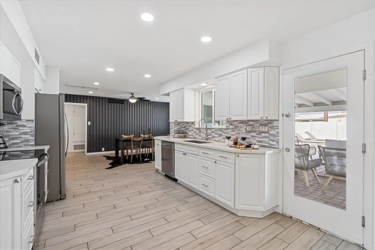 This image highlights an open kitchen island, dining area, sleek modern cabinetry, and a sliding glass door that leads directly to the backyard, all bathed in natural light. The kitchen island features bar-height seating, seamlessly connecting the cooking, dining, and social spaces.
